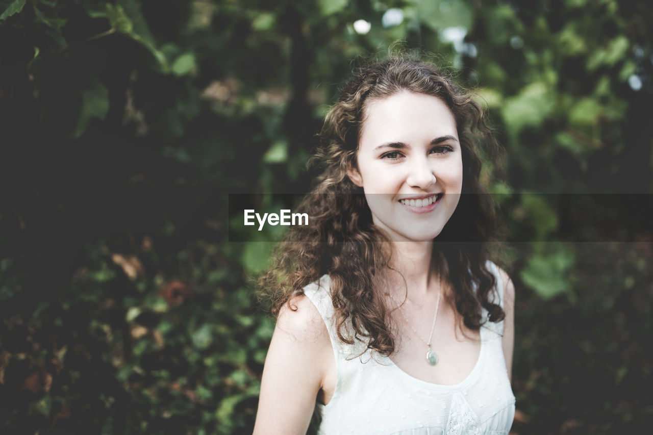 Beautiful smiling curly hair brunette in a light blue simple dress in a park