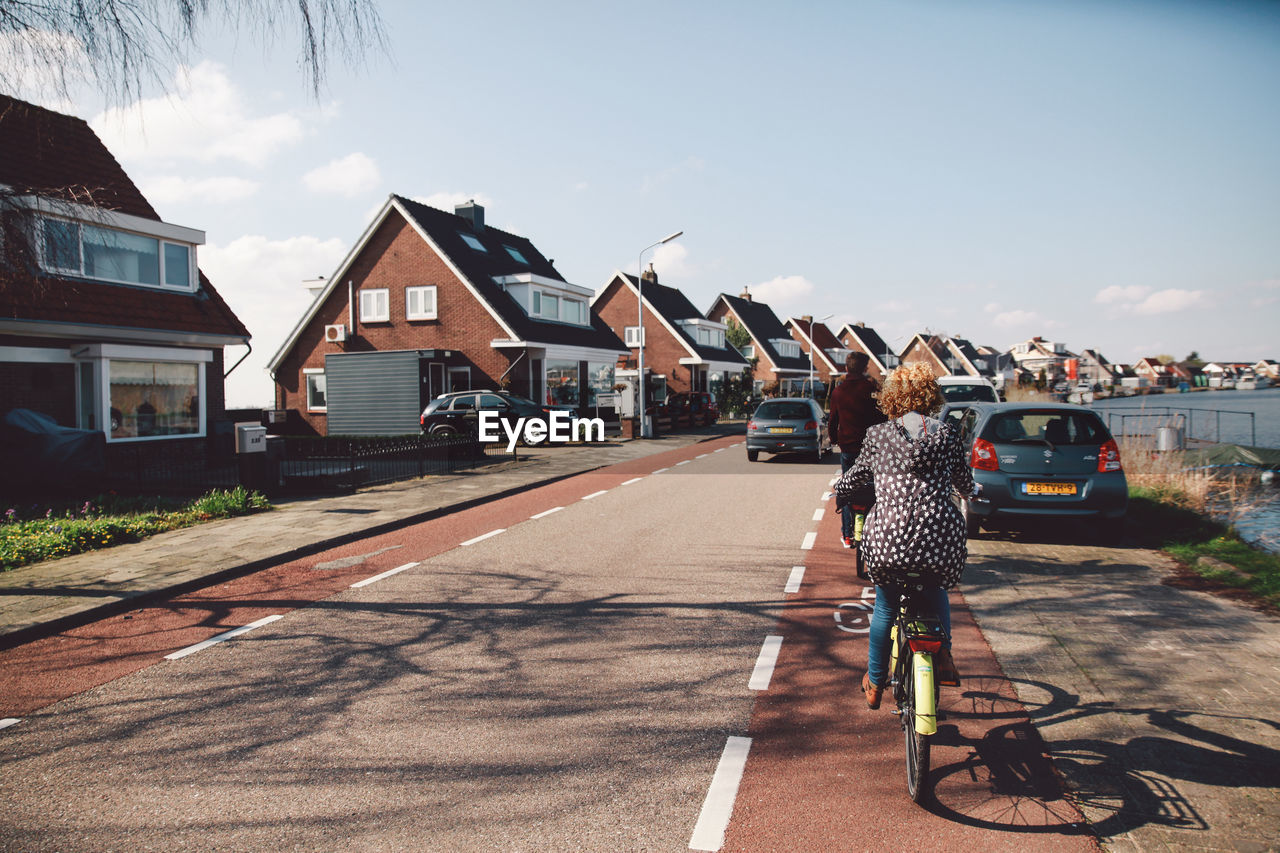 Rear view of woman riding bicycle on street against sky