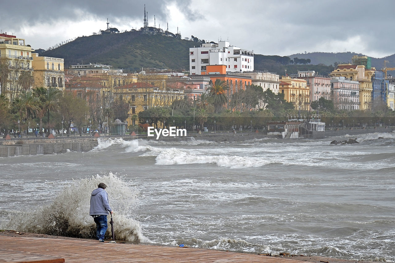 REAR VIEW OF MAN AND PEOPLE IN SEA AGAINST BUILDINGS IN CITY