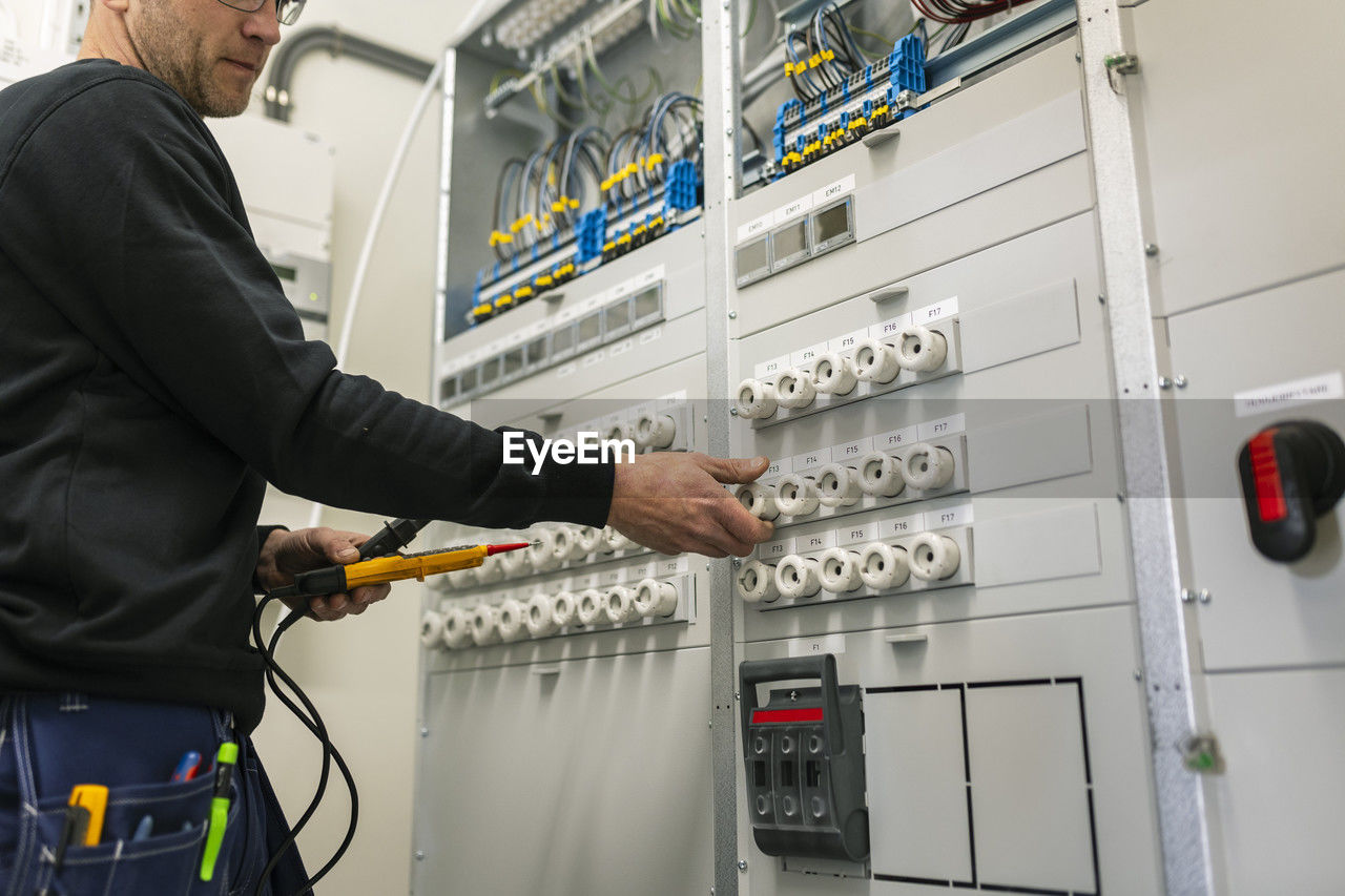 Midsection of repairman with voltage tester repairing switchboard in industry