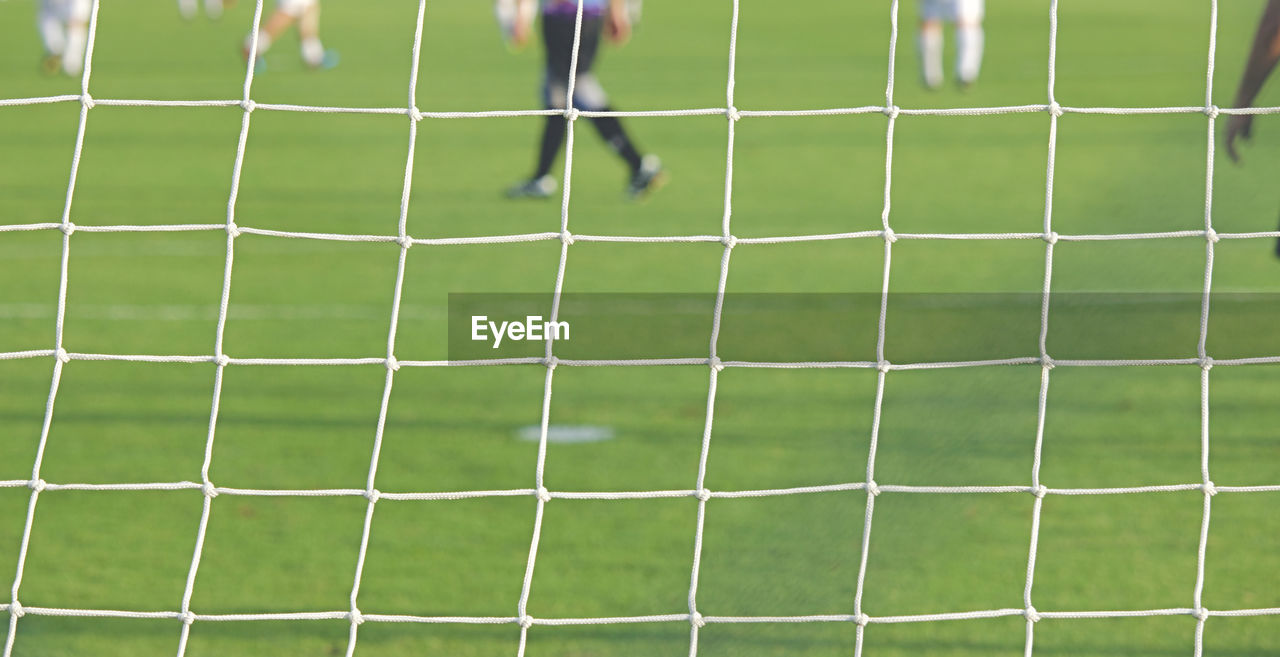 Low section of men playing soccer on field seen through goal post