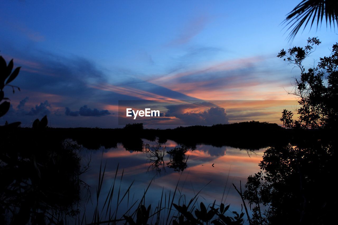 SCENIC VIEW OF LAKE AGAINST CLOUDY SKY DURING SUNSET