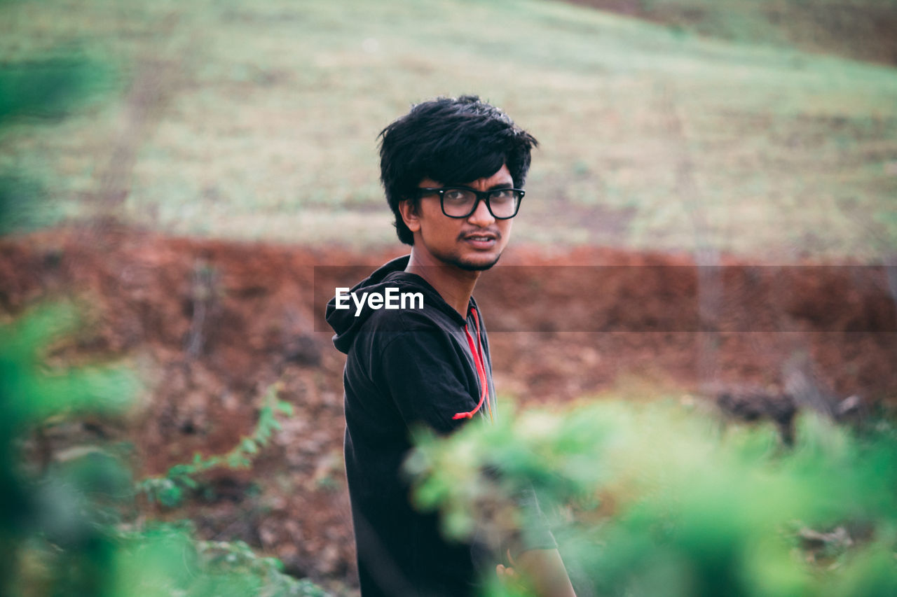 Portrait of young man wearing eyeglasses seen through plants