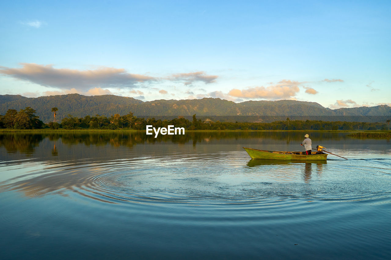 Fisherman in lake against sky