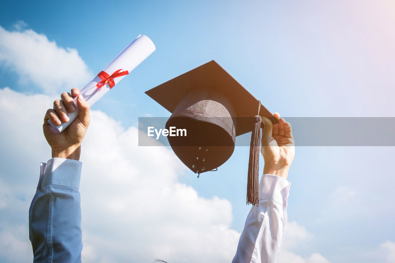 Low angle view of person hand holding certificate with mortarboard