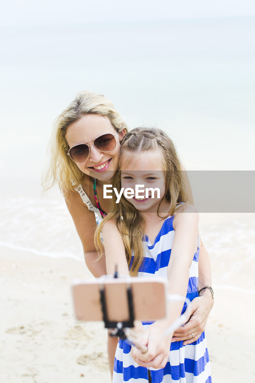 Smiling girl taking selfie with mother at beach
