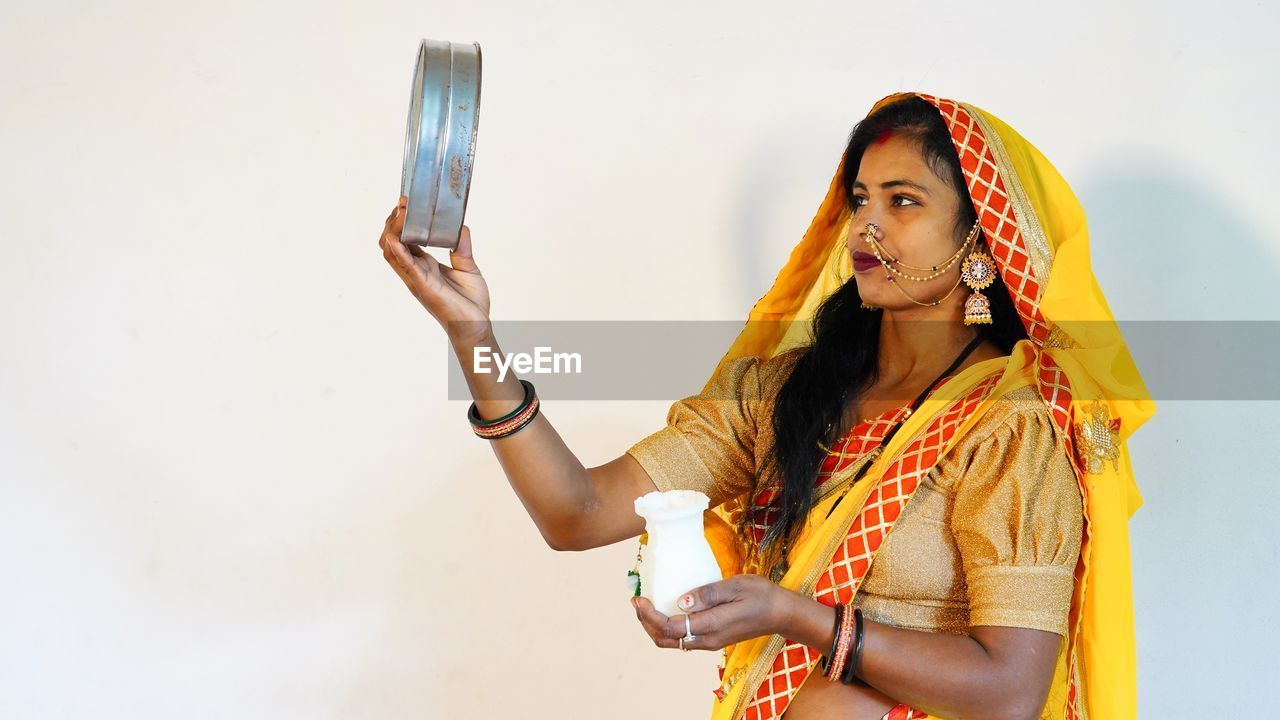 one person, yellow, adult, women, wireless technology, young adult, technology, photo shoot, mobile phone, smartphone, clothing, portable information device, portrait, holding, communication, copy space, lifestyles, person, indoors, selfie, bangle, waist up, traditional clothing, smiling, studio shot, looking, standing, female, bracelet, telephone, arts culture and entertainment, fashion, long hair, hairstyle, emotion, happiness, activity