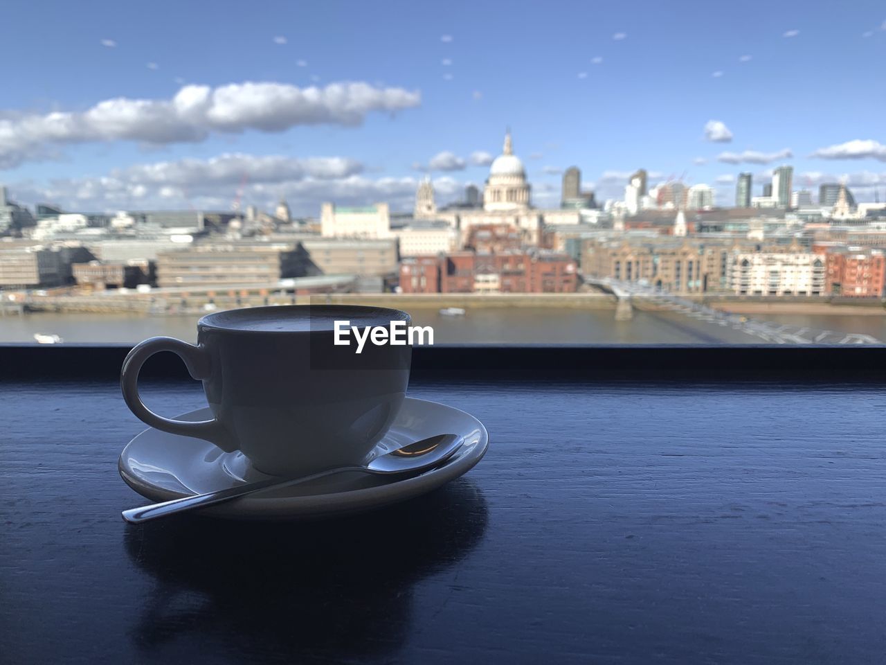 COFFEE CUP AND BUILDINGS ON TABLE AGAINST SKY
