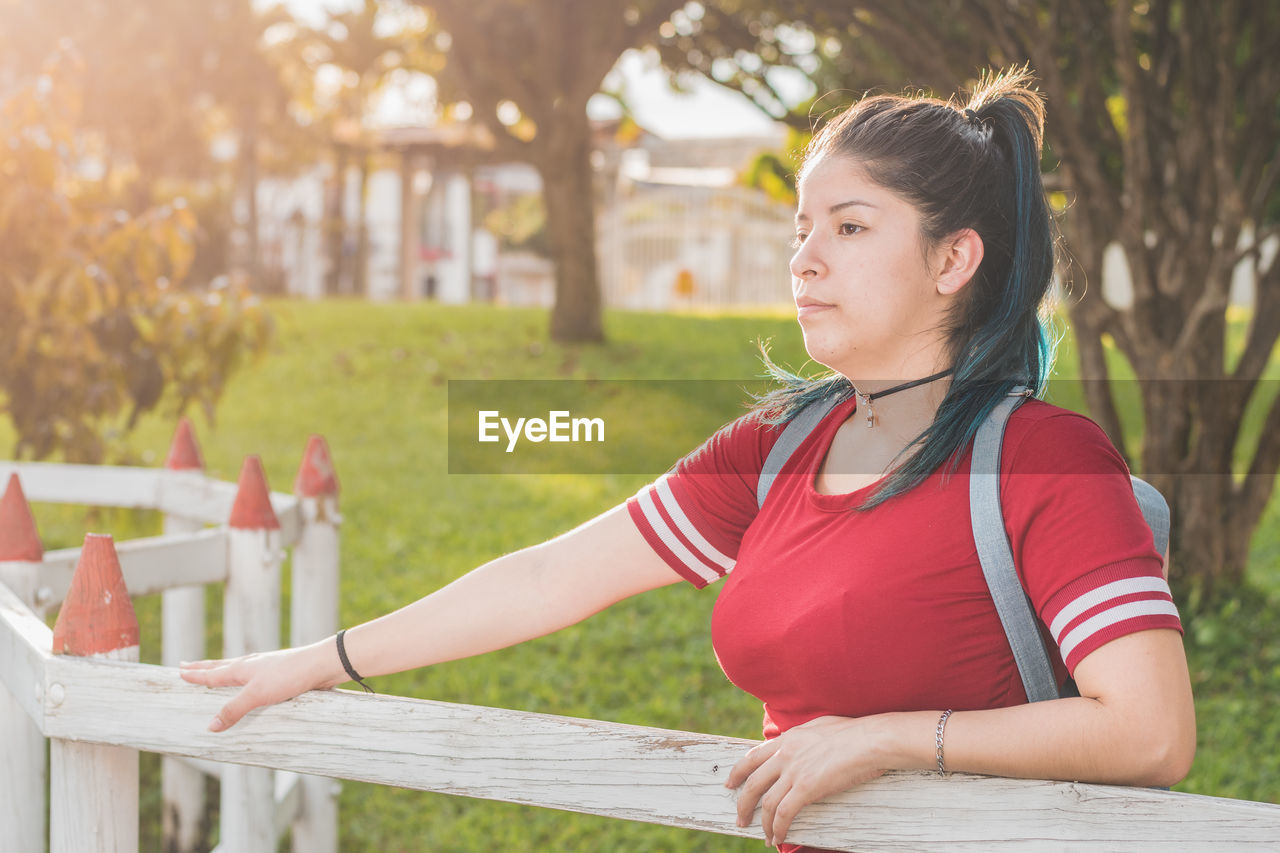 Beautiful young woman student, standing next to a wooden fence, very serious and worried about