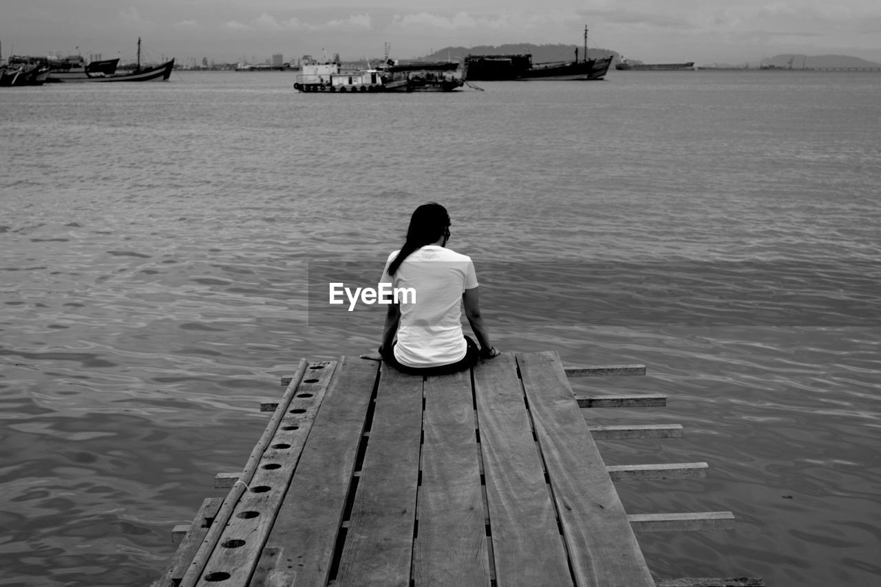 Rear view of man sitting on pier over river