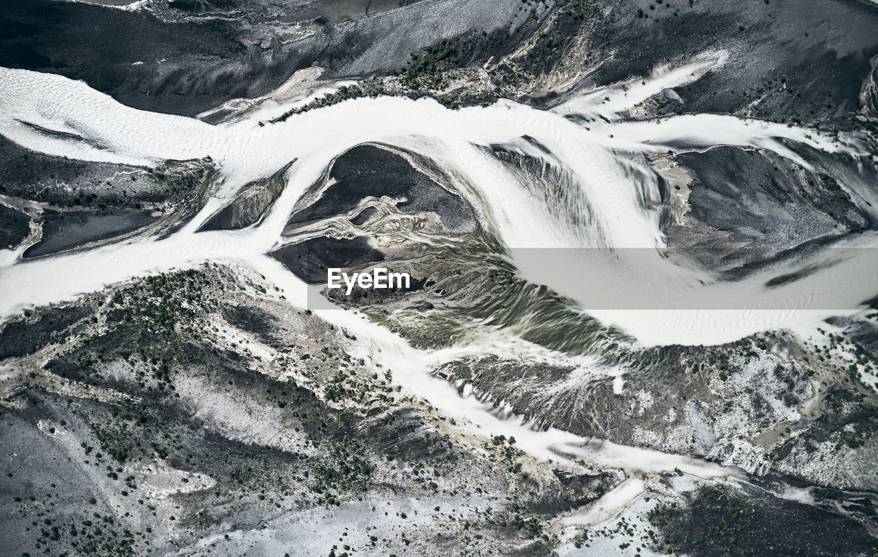 Frozen river streams twisting around pool in mountains