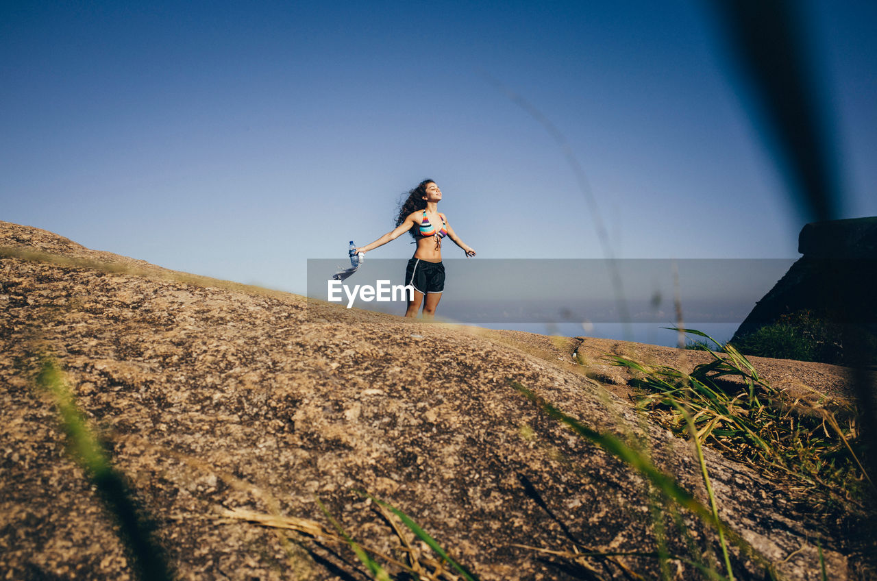 Young woman standing in field against clear sky