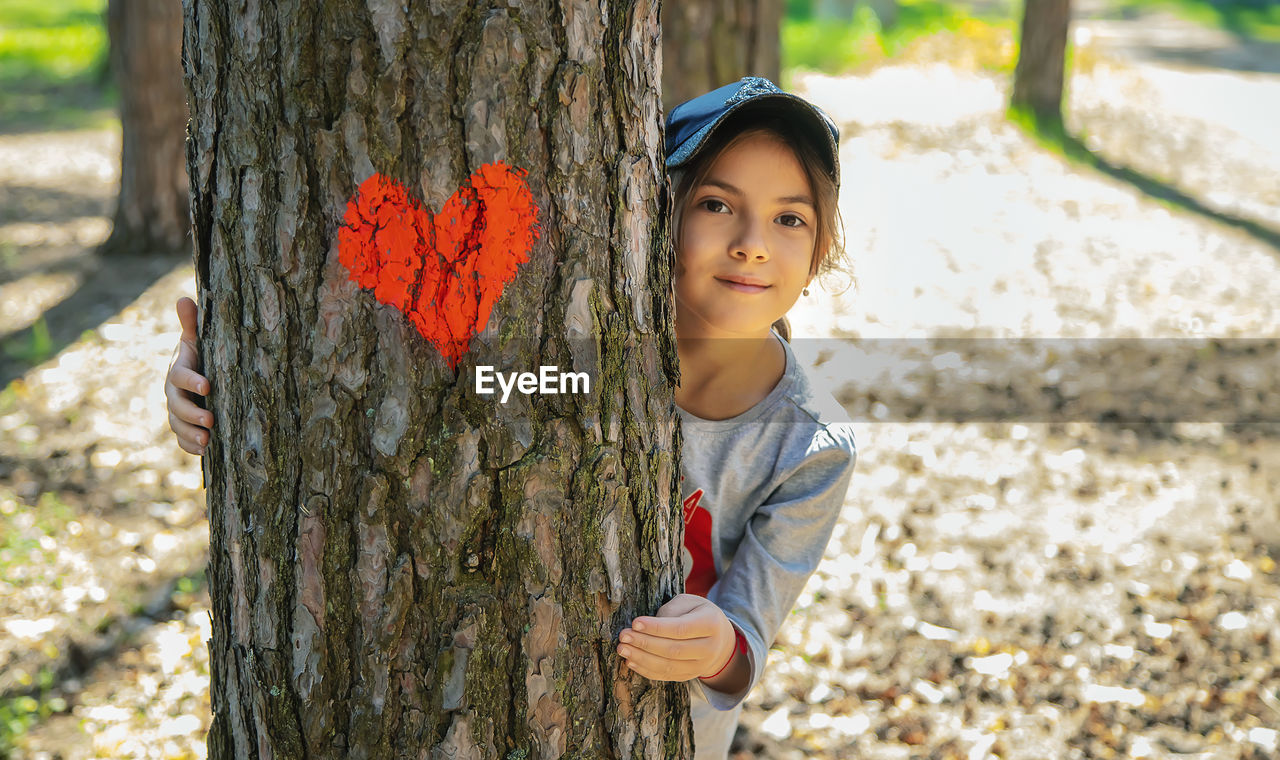 portrait of smiling young woman standing by tree trunk