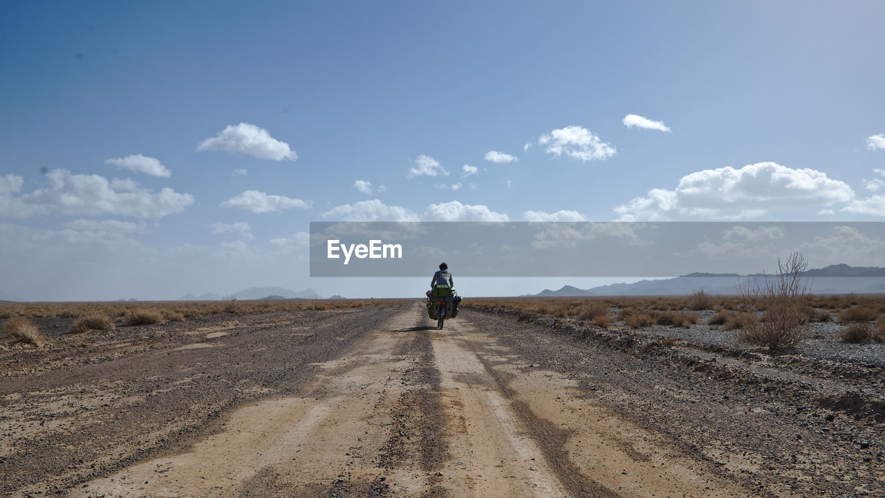 Rear view of man riding motorcycle on road against sky