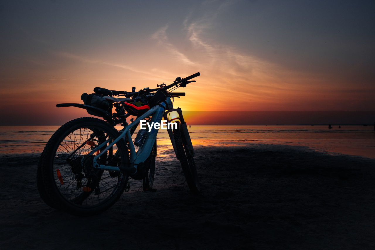 Bicycle on beach against sky during sunset