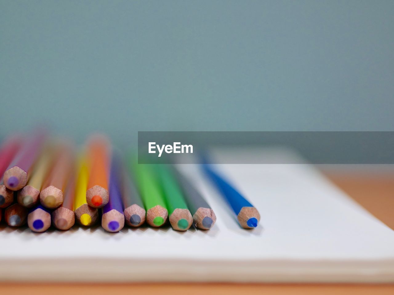 Close-up of colored pencils on book against wall