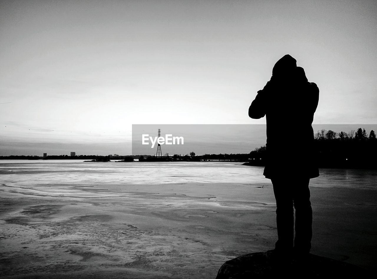 Silhouette of person standing on stone against frozen landscape
