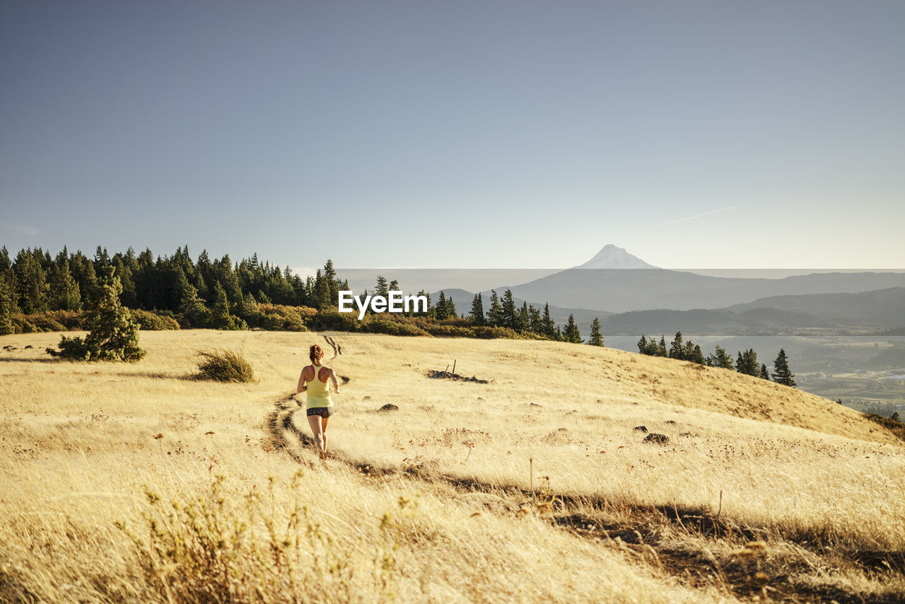 Rear view of woman jogging on mountain against sky during sunny day