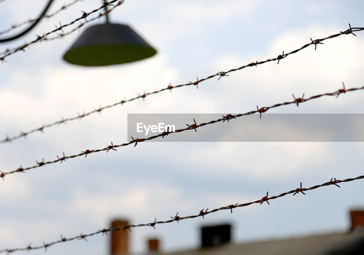 Close-up of barbed wire fence against sky