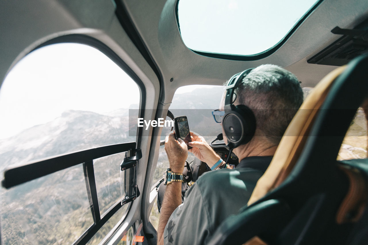 Retired man takes photo with phone from inside helicopter.
