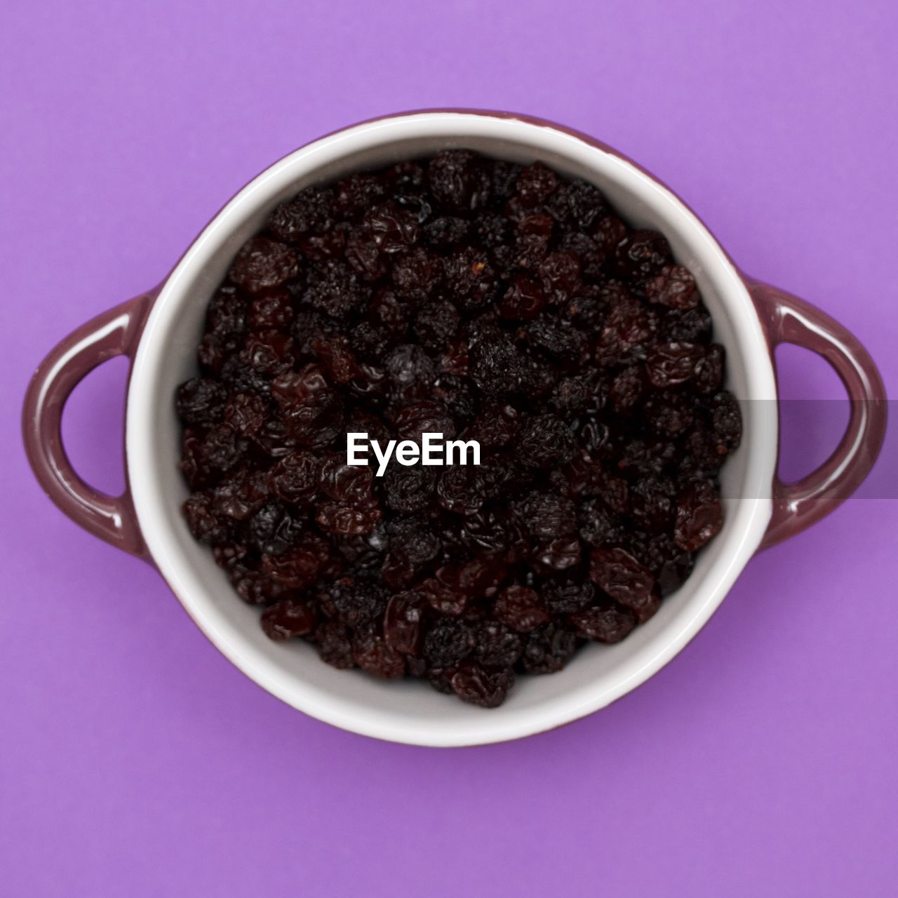 Directly above shot of raisins in bowl over purple background