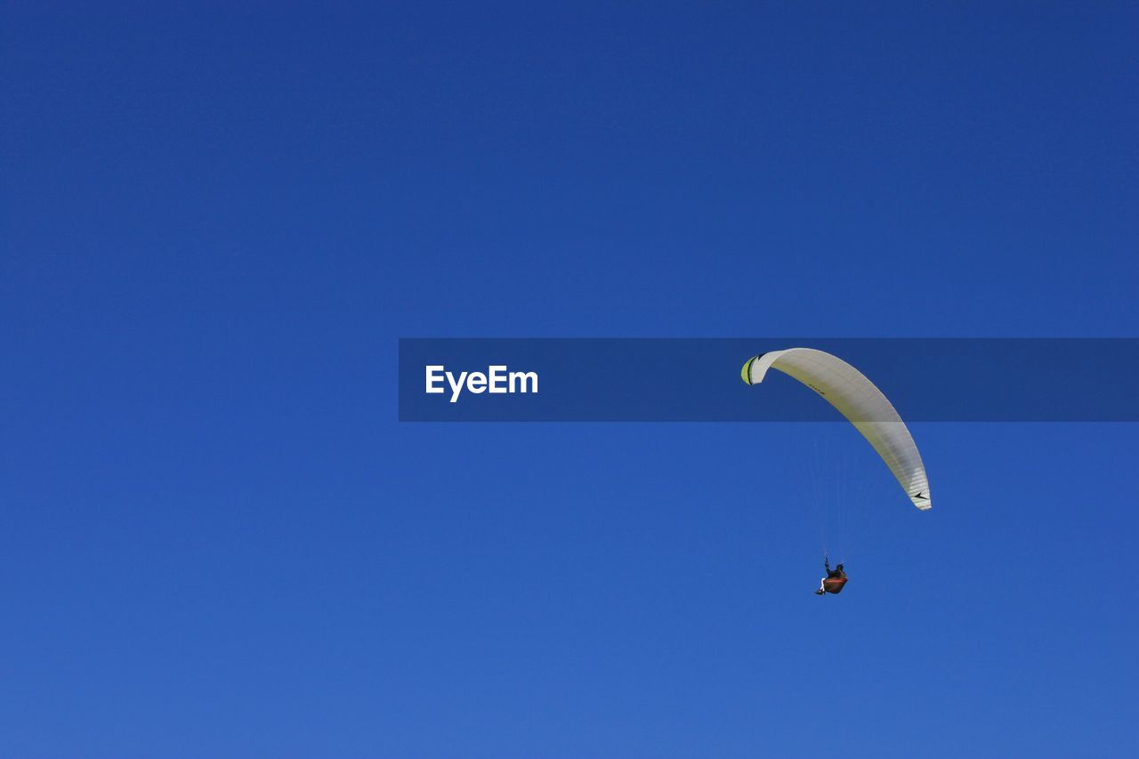 Low angle view of young man paragliding against clear blue sky