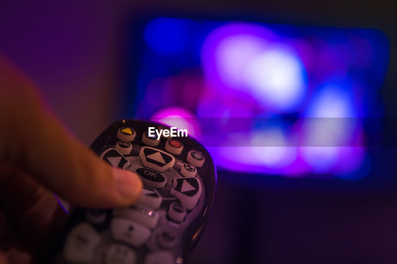 Cropped image of hand holding remote control in front of television set