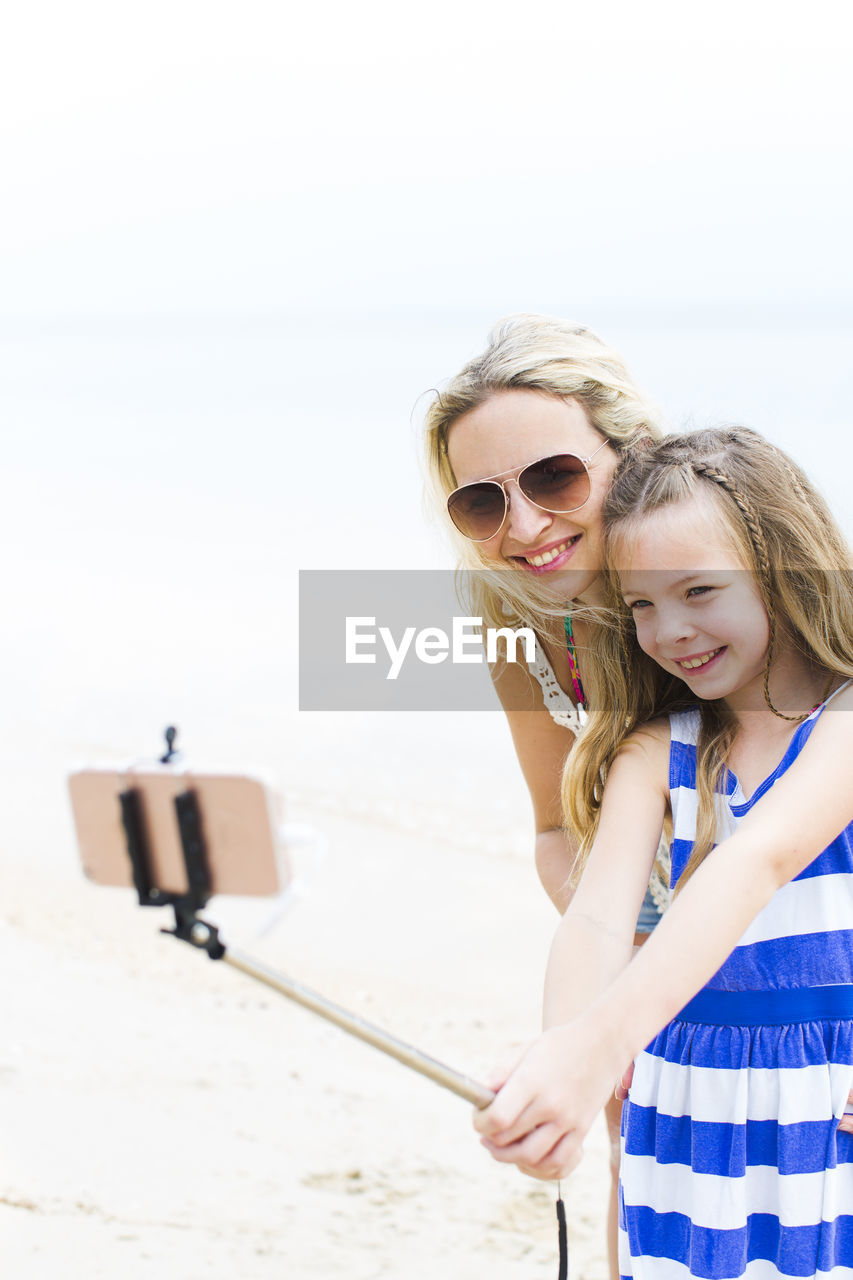 Smiling girl taking selfie with mother at beach