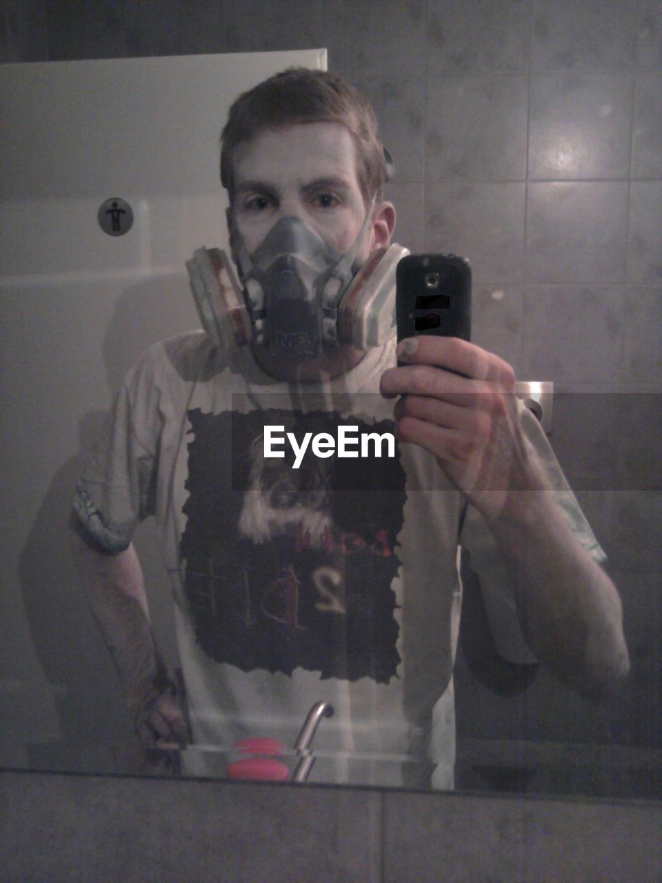 Reflection of man wearing gas mask on mirror while taking selfie in bathroom