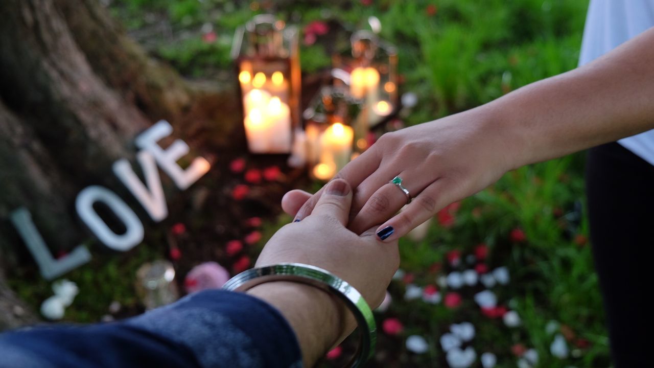 Cropped image of couple holding hands by candles on field