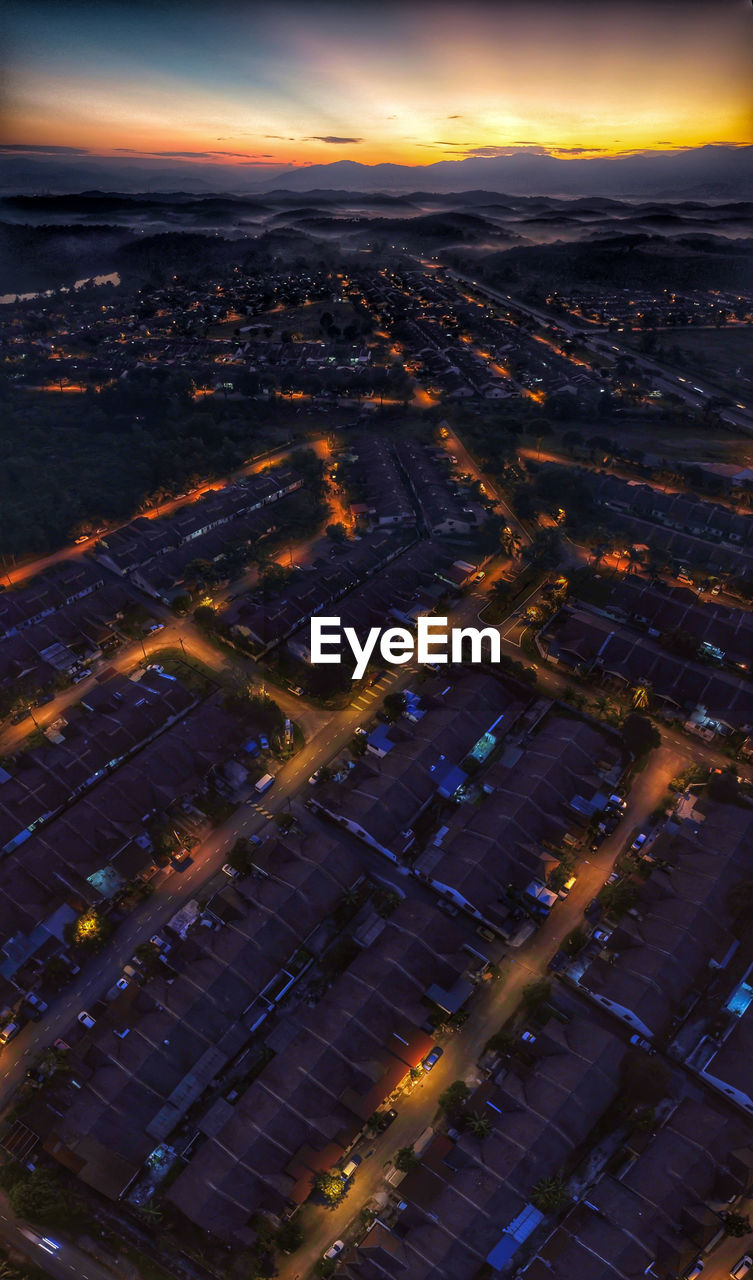 High angle view of illuminated city buildings against sky at sunset