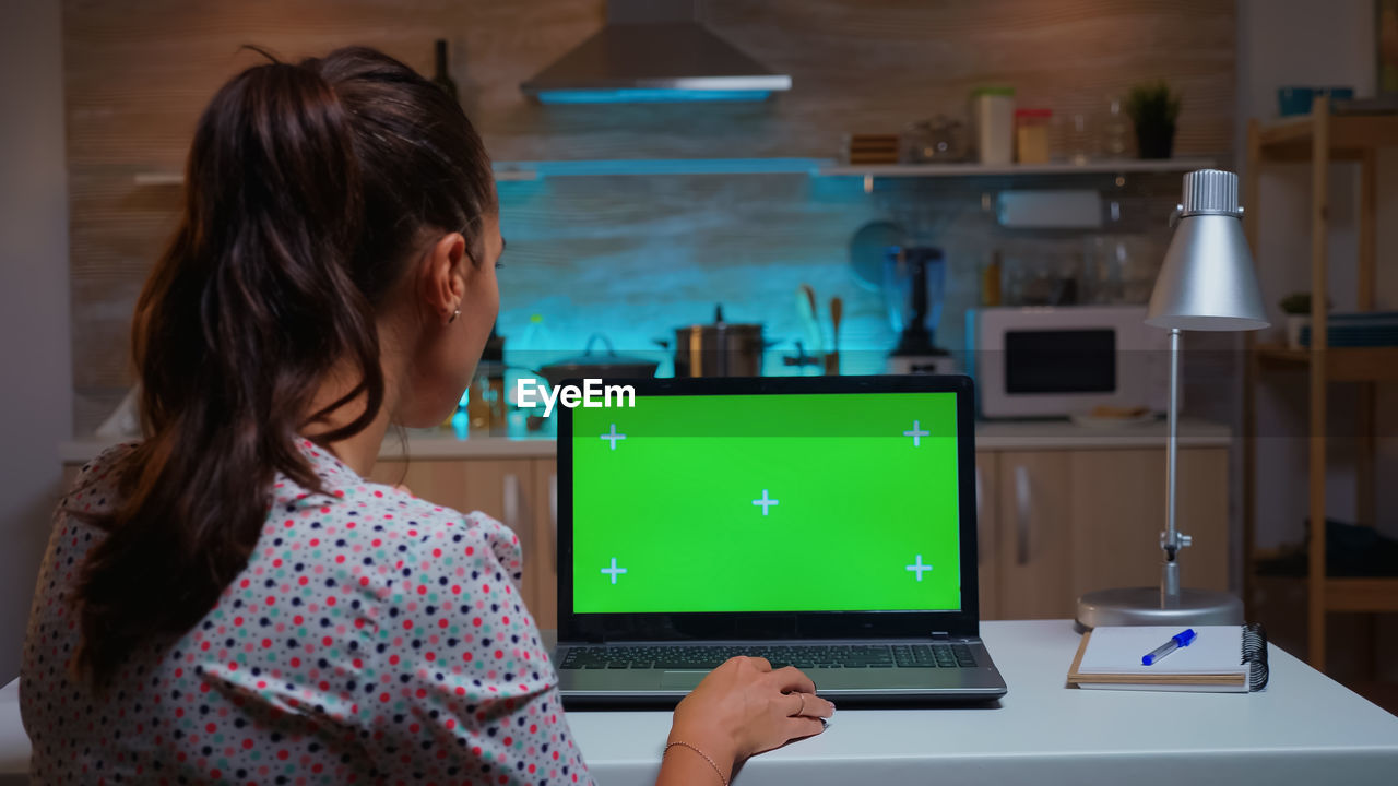 rear view of young woman using laptop on table at home