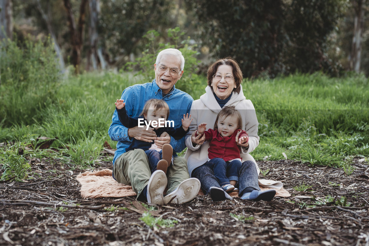 Portrait of senior active couple holding twin granddaughters outside