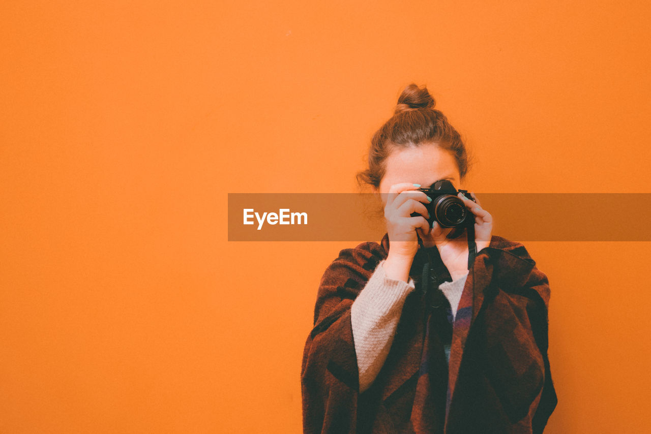 Front view of woman photographing against orange background