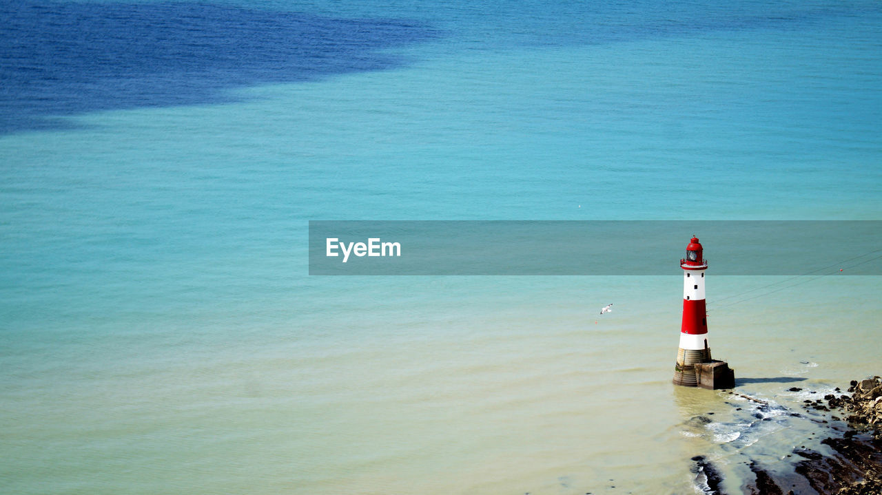Lighthouse on beach by sea against sky