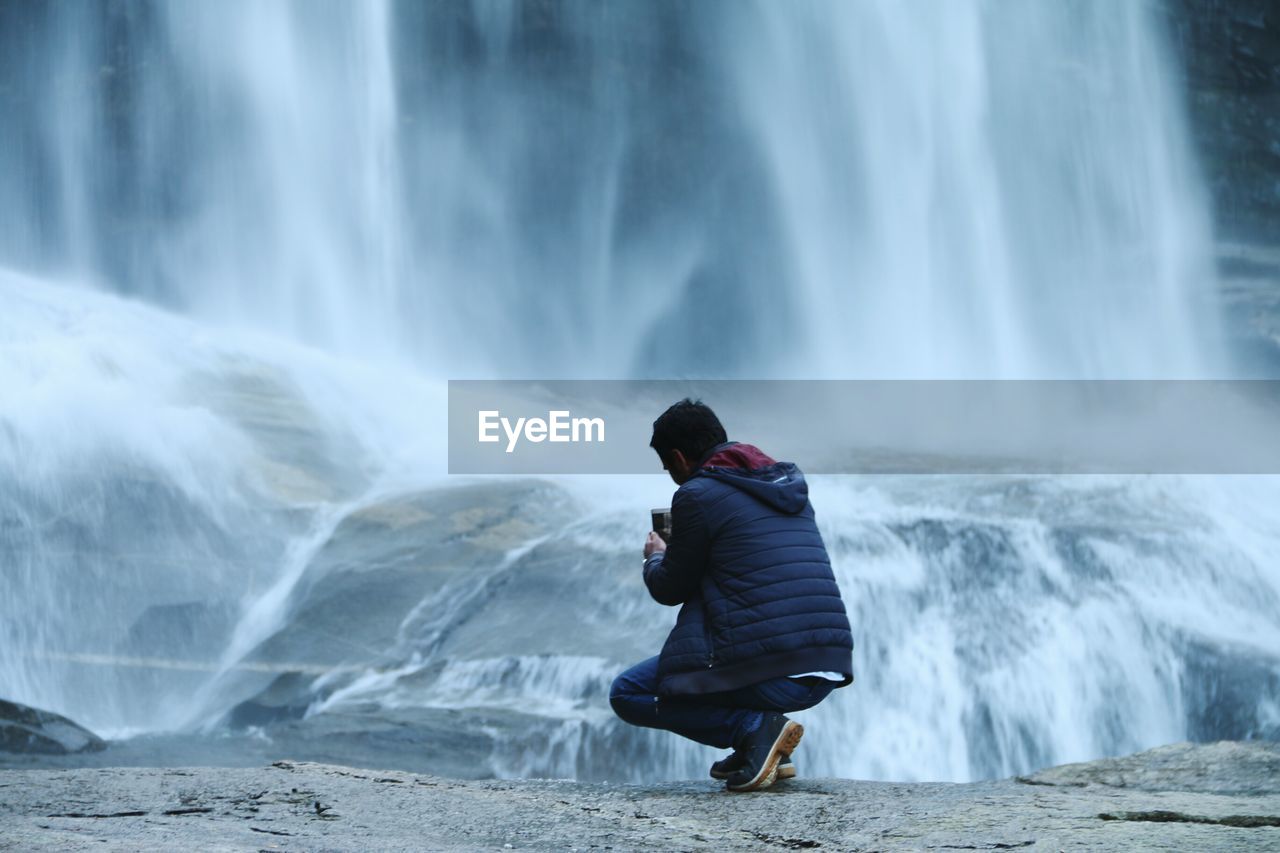 Rear view of man photographing waterfall