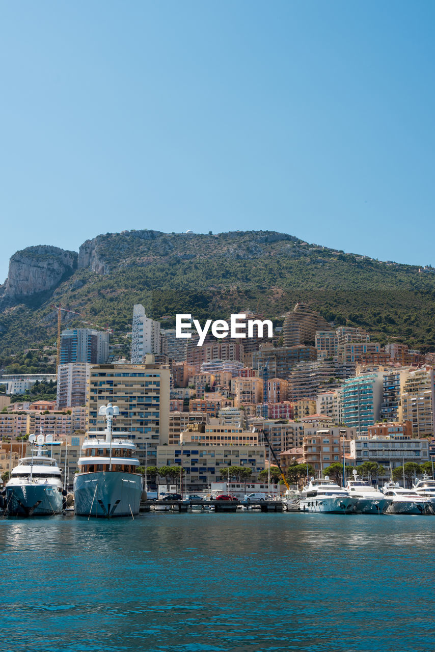 Cityscape by sea against clear blue sky