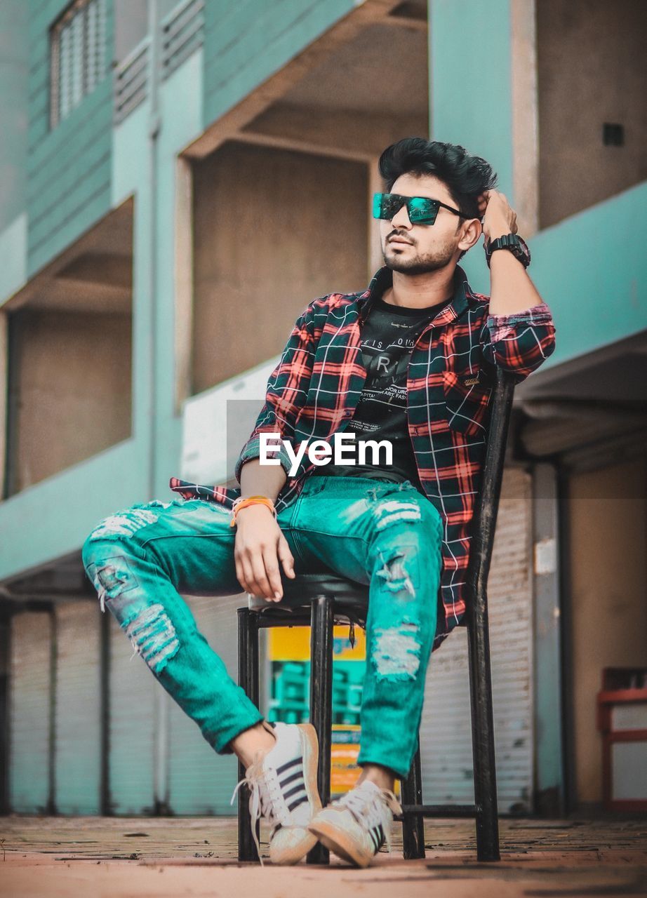 FULL LENGTH PORTRAIT OF YOUNG MAN SITTING ON WALL