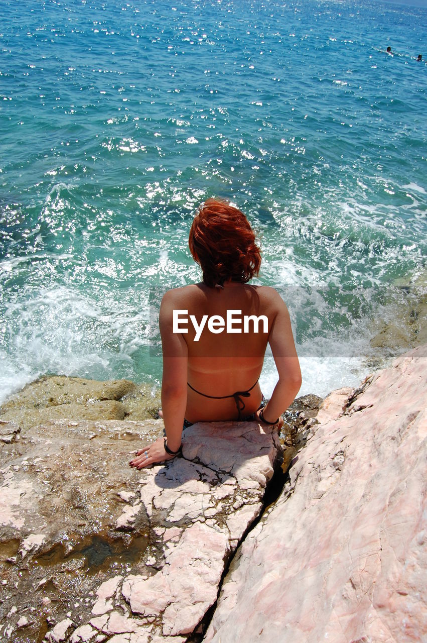 Rear view of woman sitting on rock by sea