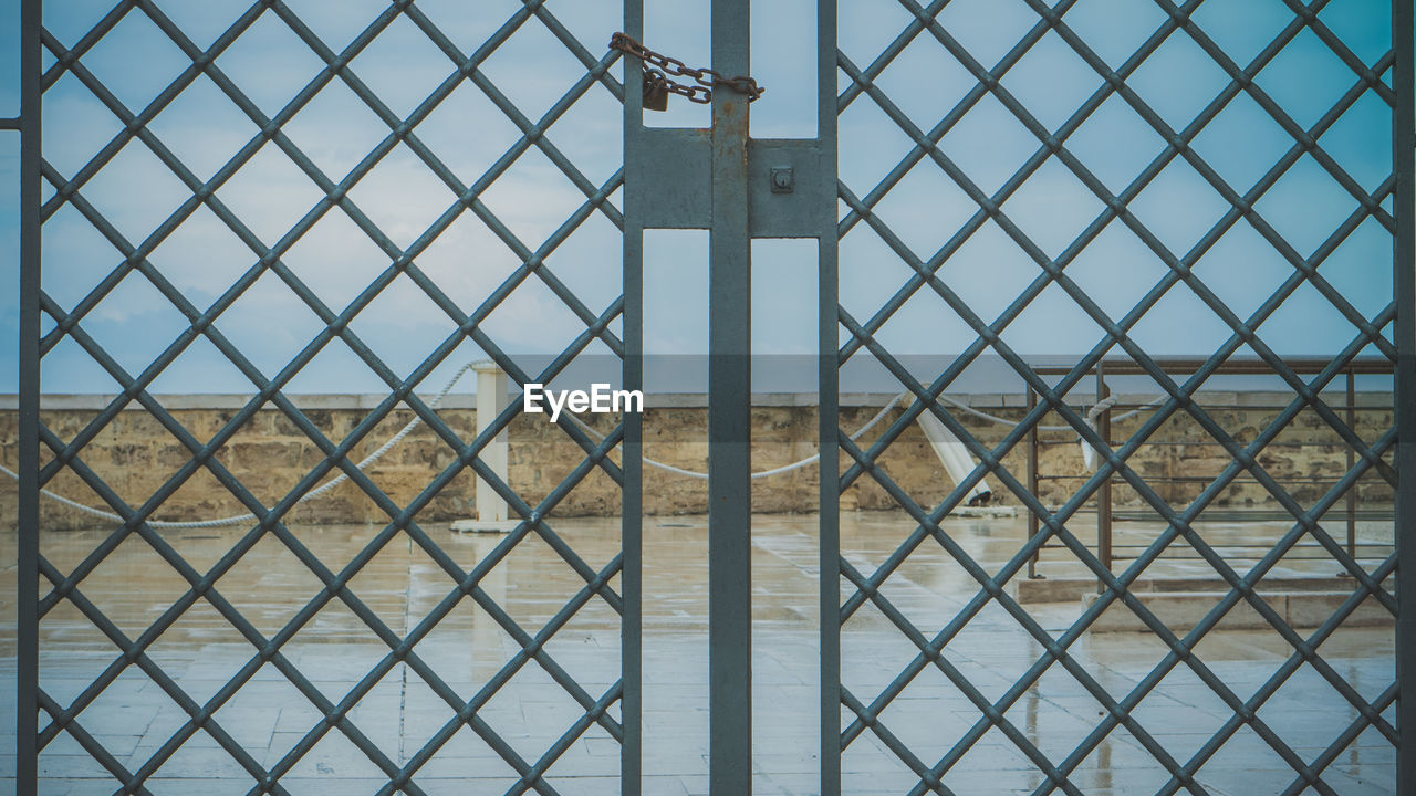 CHAINLINK FENCE AGAINST SKY SEEN THROUGH METAL RAILING