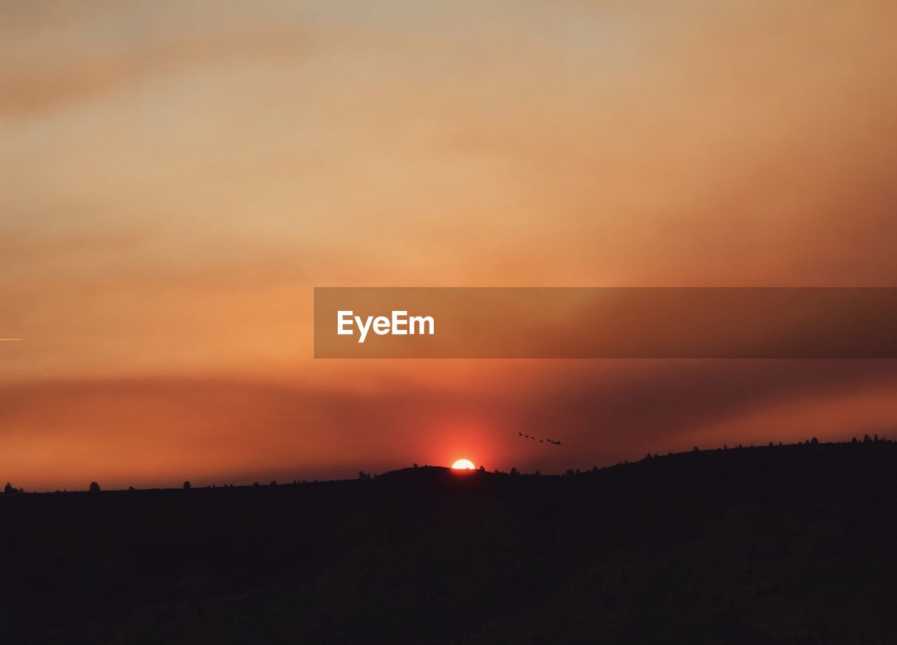 Scenic view of silhouette landscape against orange sky