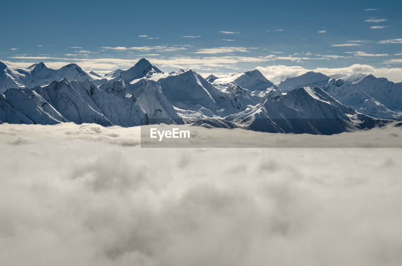 Scenic view of cloudscape by snow covered mountains against sky