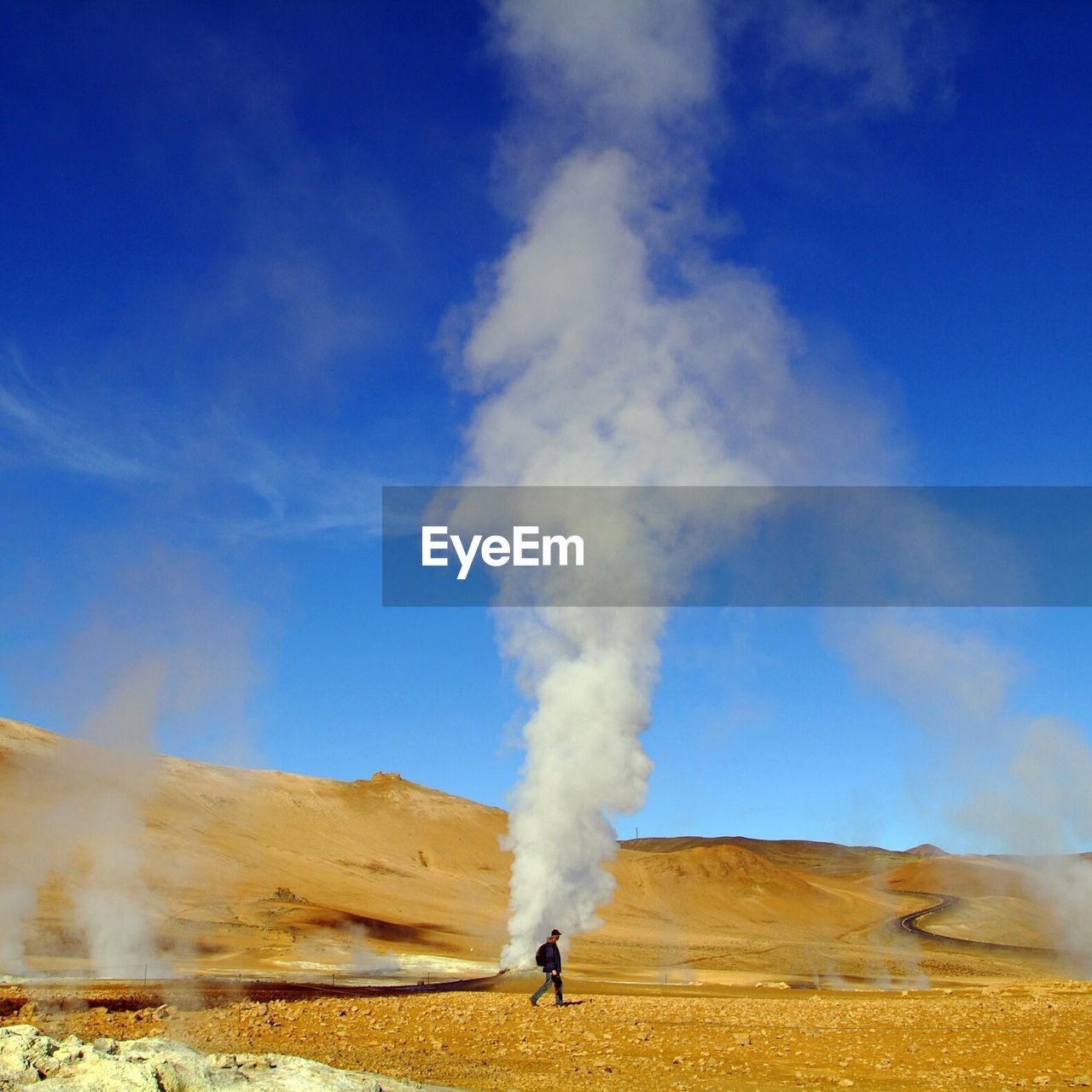 Man walking by hot spring against blue sky on sunny day