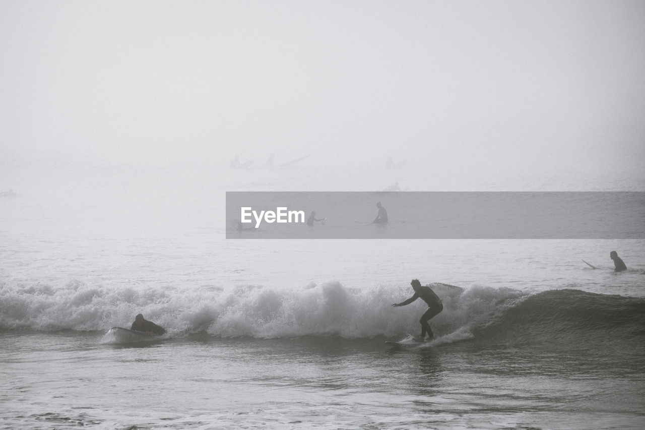 People surfboarding in sea during foggy weather