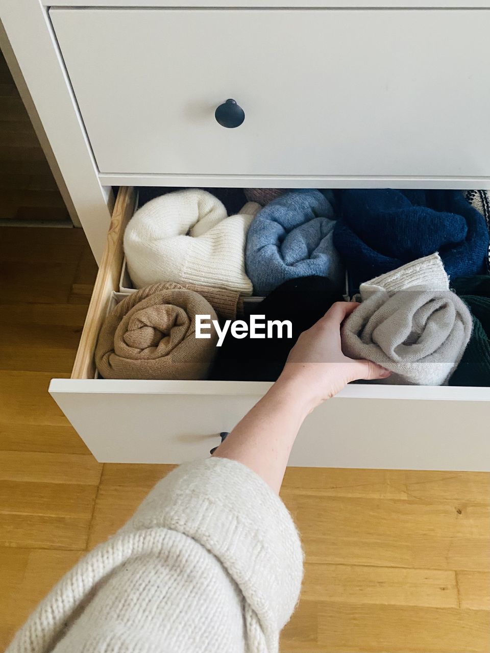 Organized dresser drawer and a human hand reaching for a sweater 