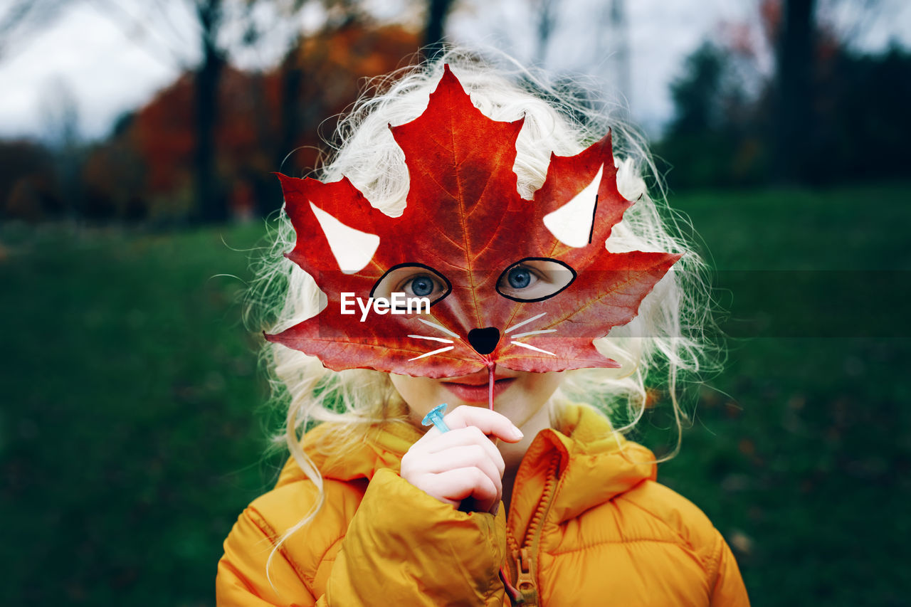 Portrait of girl holding maple leaf at park