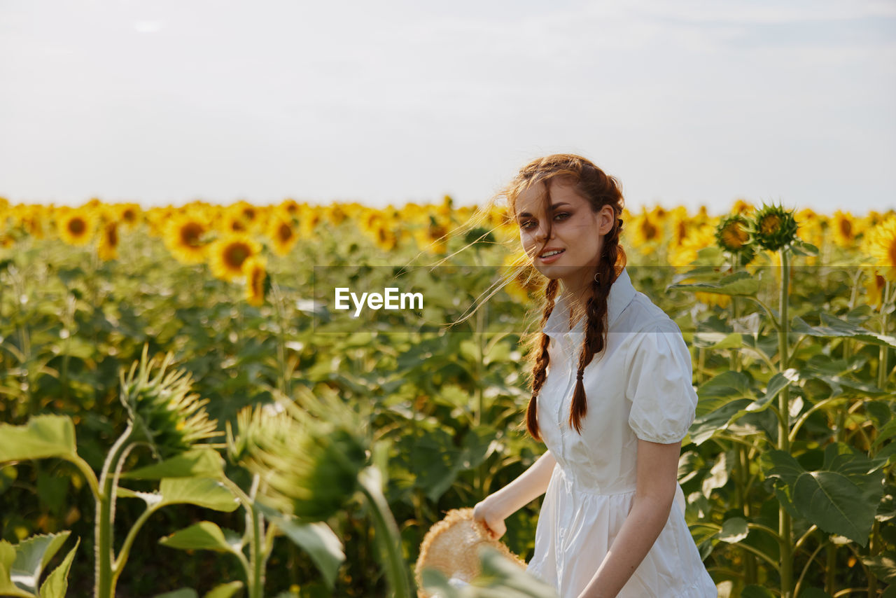 portrait of smiling young woman standing by flowering plant