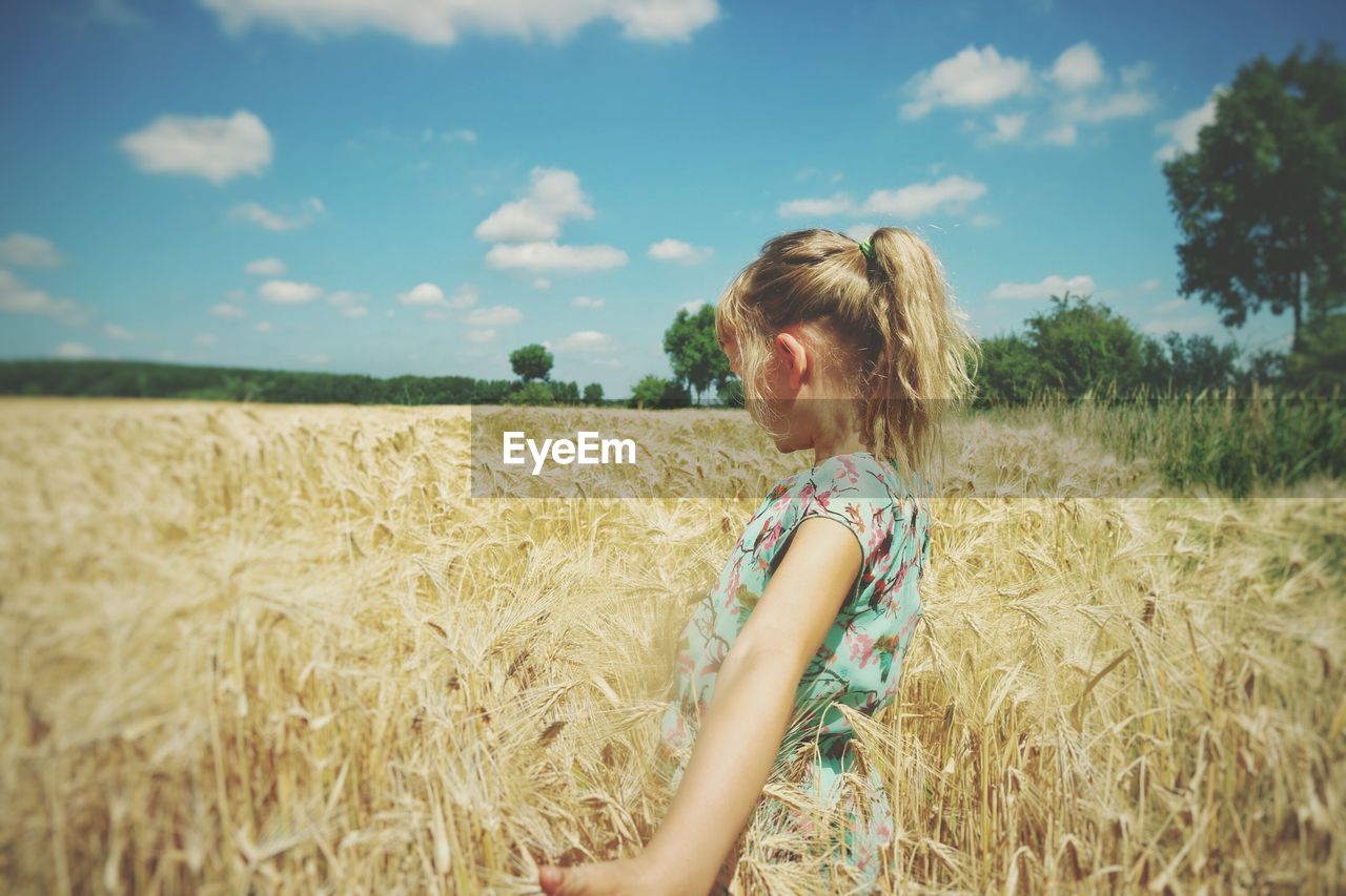 Side view of girl standing in wheat field against sky
