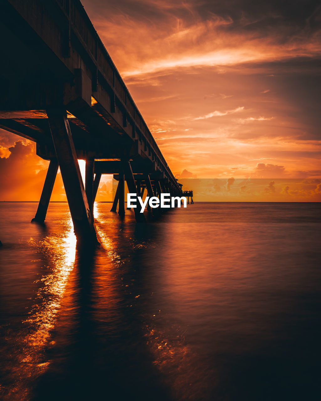 Silhouette pier over sea against orange sky