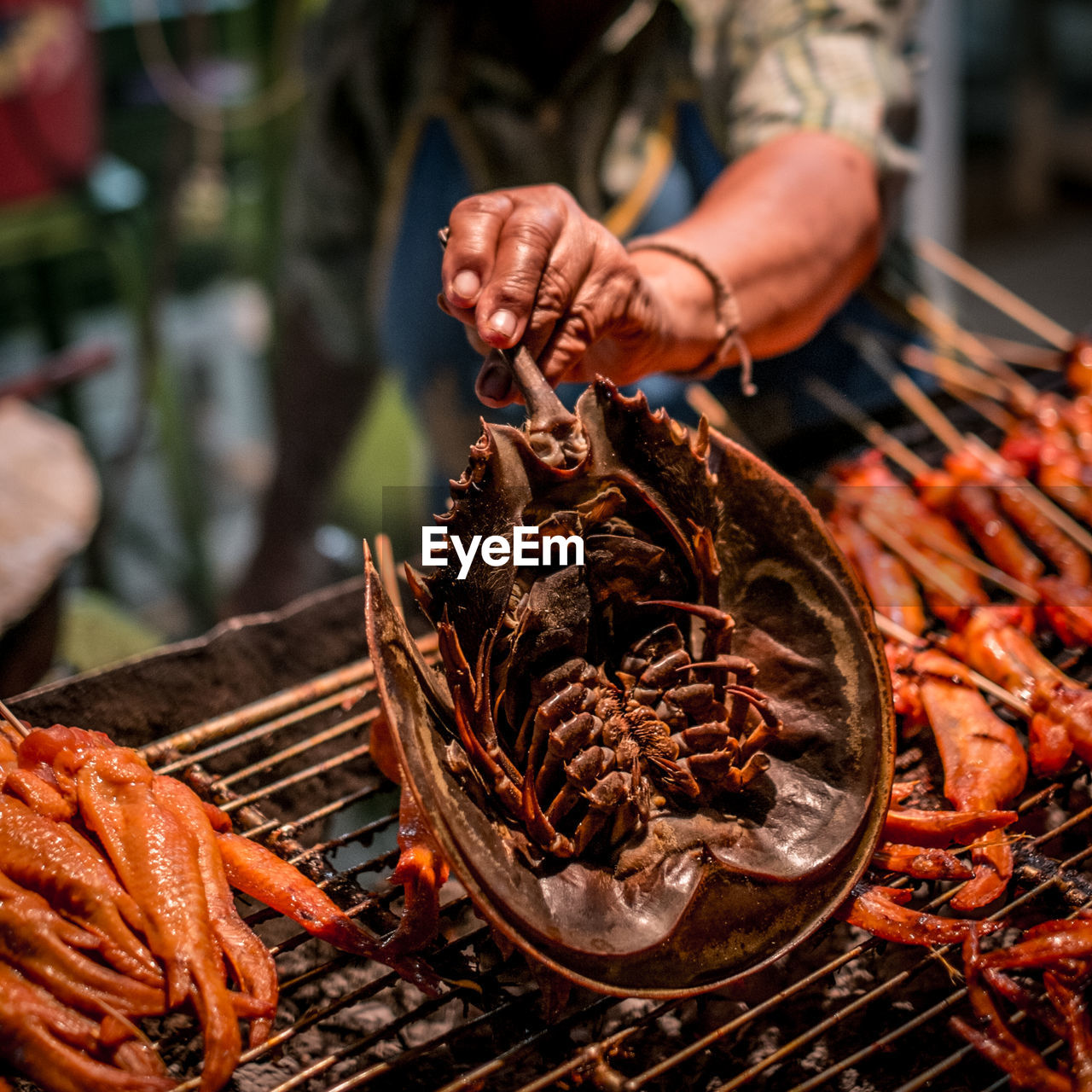 Midsection of vendor cooking seafood on barbecue grill
